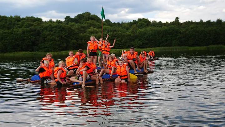 Glade spejdere i orange redningsveste på deres egen selvbyggede tømmerflåde på flot sø ved sommerlejren 2018